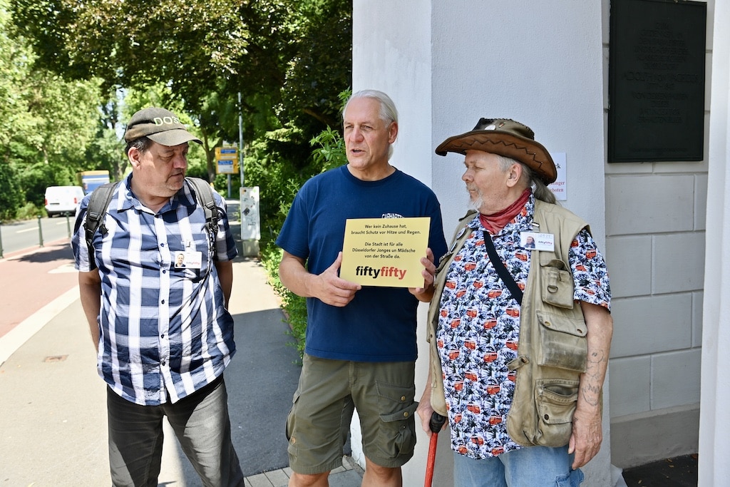 Helmut (v.l.) vom Straßenmagazin Fiftyfifty, Streetworker Oliver Ongaro und Django hängten am Mittwoch ein neues Schild am Ratinger Tor auf. © Lokalbüro